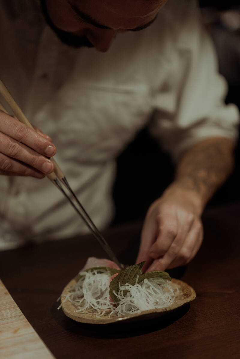Chef preparando un plato con palillos y hoja de shiso