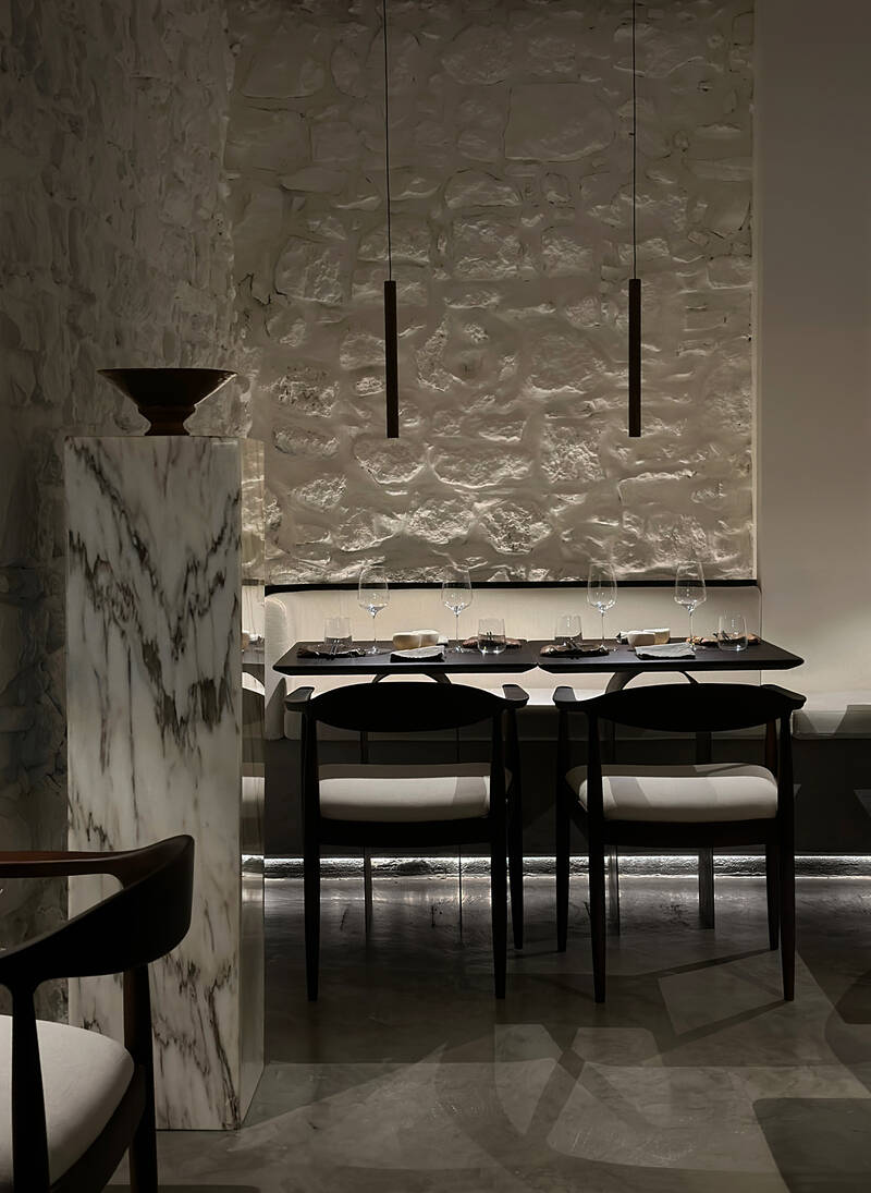 Interior del restaurante MA con mesa, pared de piedra y lámparas colgantes