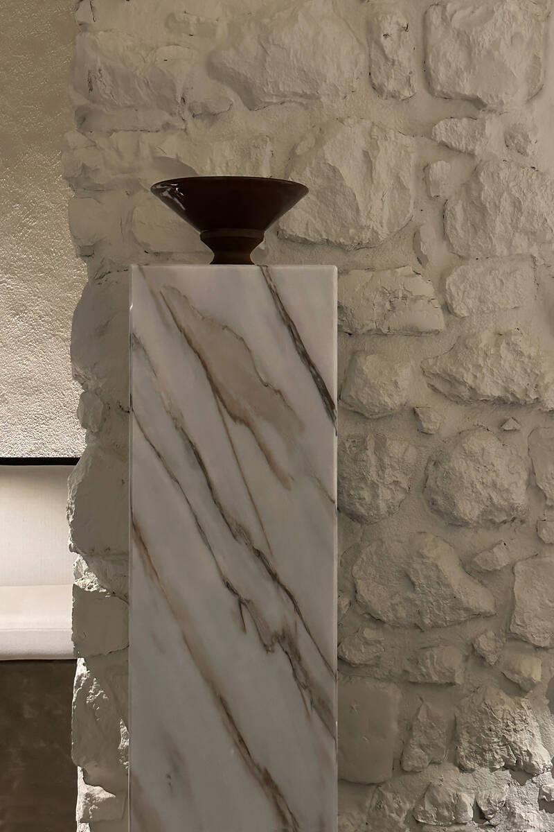 Pieza de cerámica en pedestal de mármol junto a pared de piedra